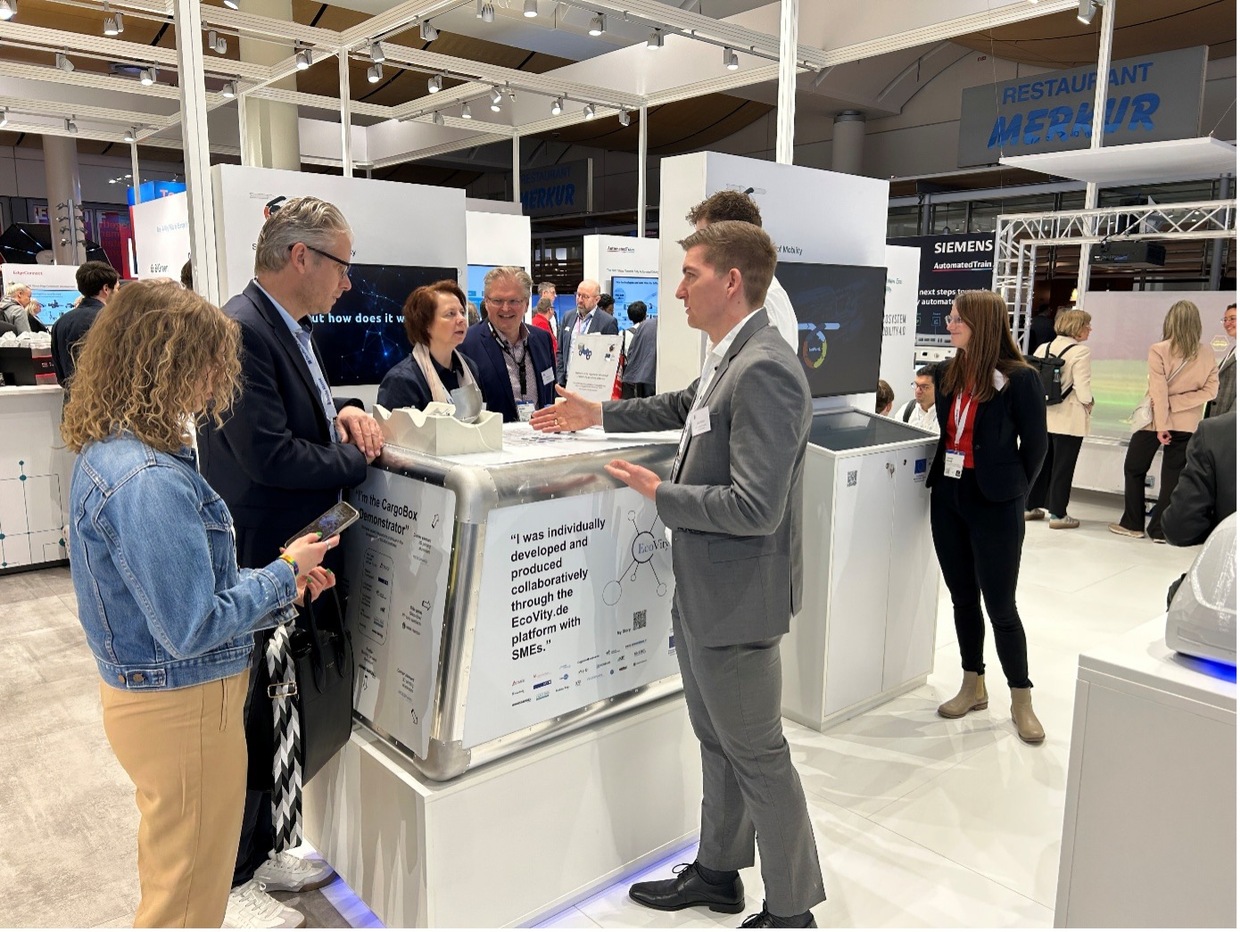 Stand mit CargoBox Demonstrator auf einer Messe, umgeben von Besuchern und Fachleuten.